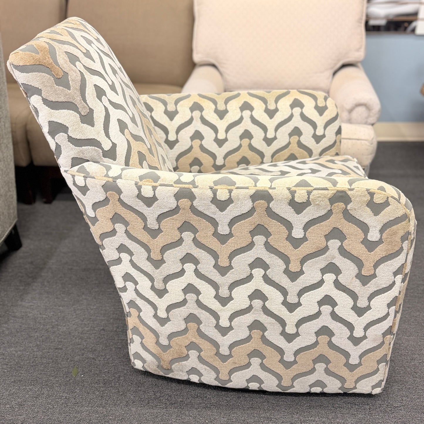 A fully upholstered swivel armchair featuring a wavy geometric chevron pattern in shades of grey, beige, and tan.