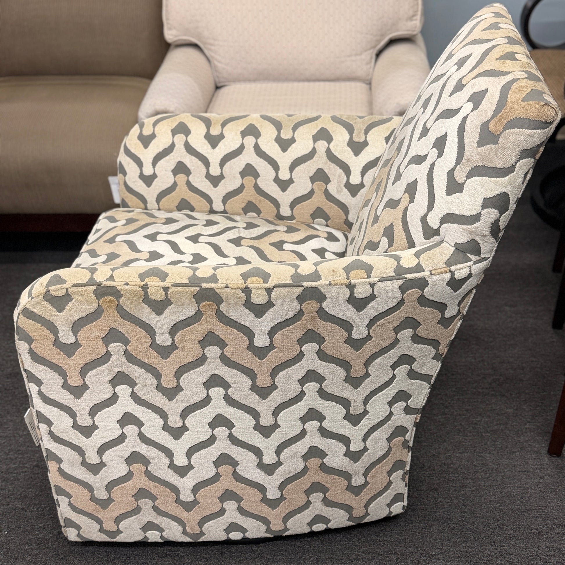 A fully upholstered swivel armchair featuring a wavy geometric chevron pattern in shades of grey, beige, and tan.