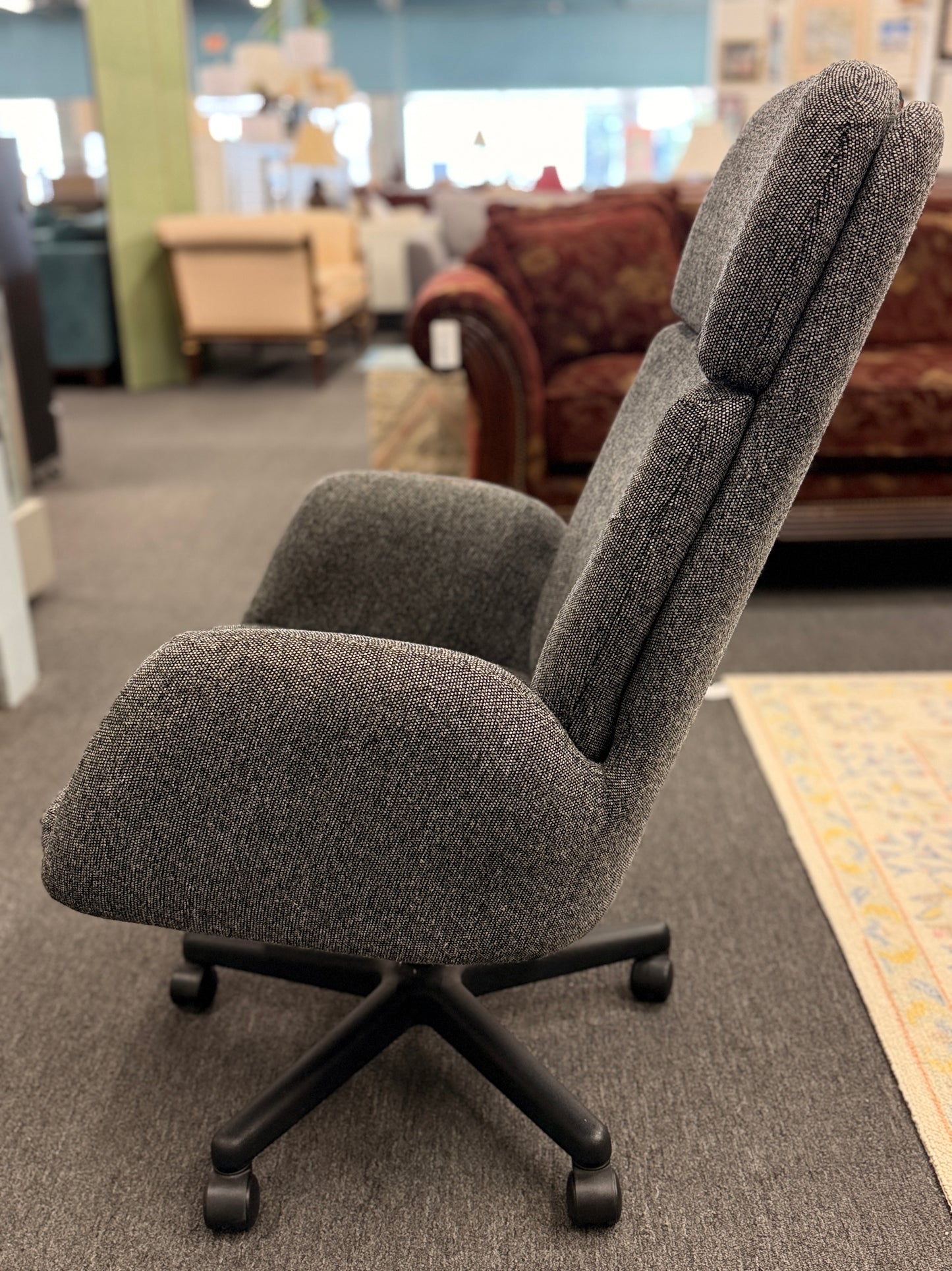 A modern minimalist high-back swivel office chair upholstered in textured grey fabric on a dark five-point wheeled base.