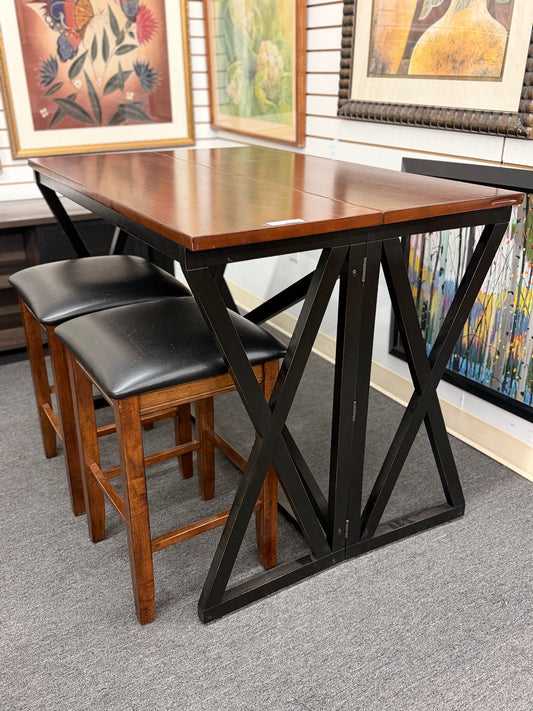 A counter-height dining set featuring a warm wood drop-leaf top, black metal X-frame base, and two matching backless barstools with black faux-leather cushioned seats in good condition.