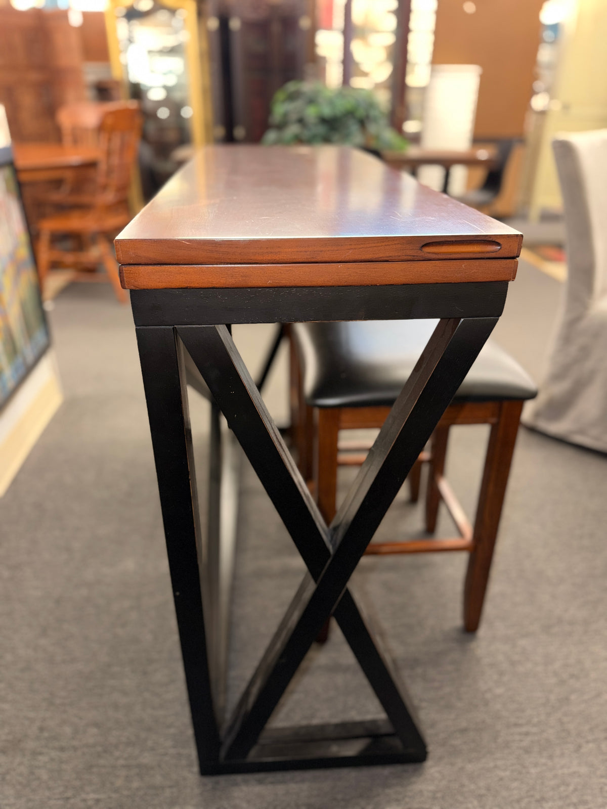 A counter-height dining set featuring a warm wood drop-leaf top, black metal X-frame base, and two matching backless barstools with black faux-leather cushioned seats in good condition.