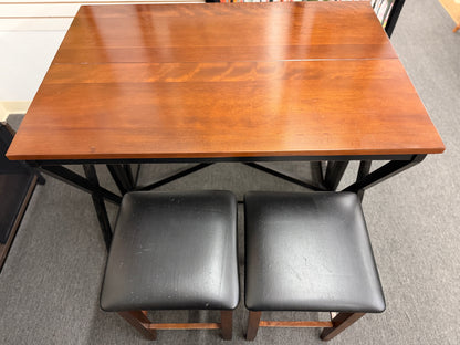 A counter-height dining set featuring a warm wood drop-leaf top, black metal X-frame base, and two matching backless barstools with black faux-leather cushioned seats in good condition.