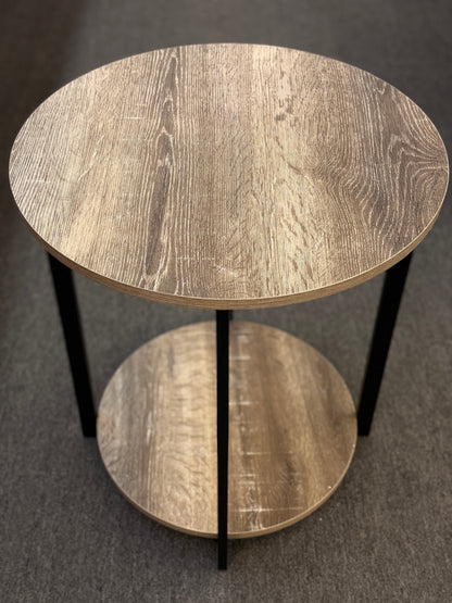 A round two-tiered end table featuring a distressed faux wood-grain finish on both circular shelves with a minimalist black iron frame.