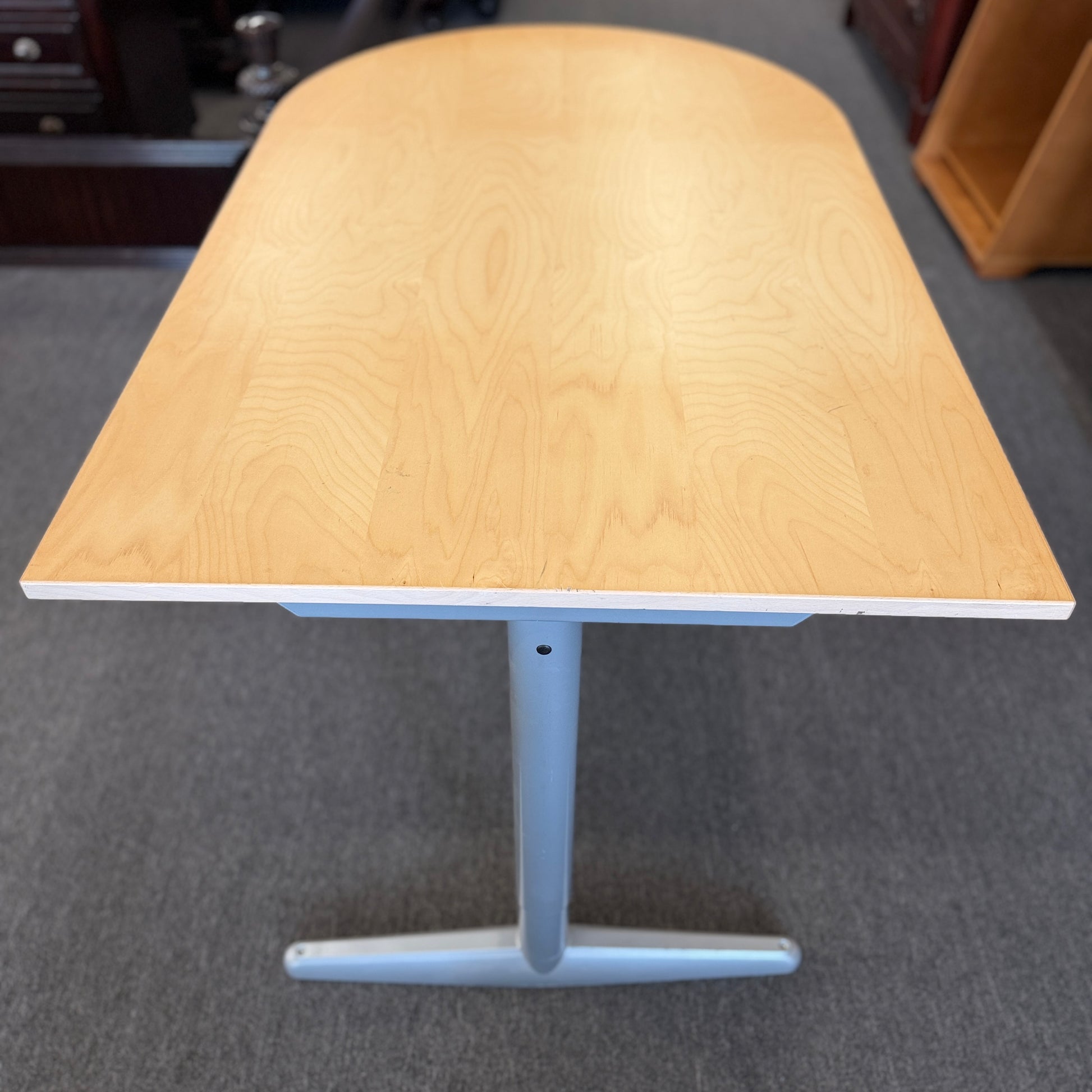 Modern office desk with a light wood D-shaped desktop, angled gray metal legs, and wide stabilizing feet.