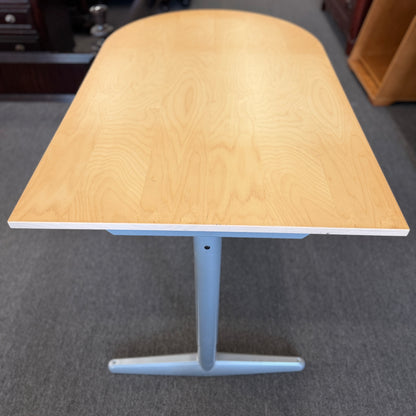 Modern office desk with a light wood D-shaped desktop, angled gray metal legs, and wide stabilizing feet.
