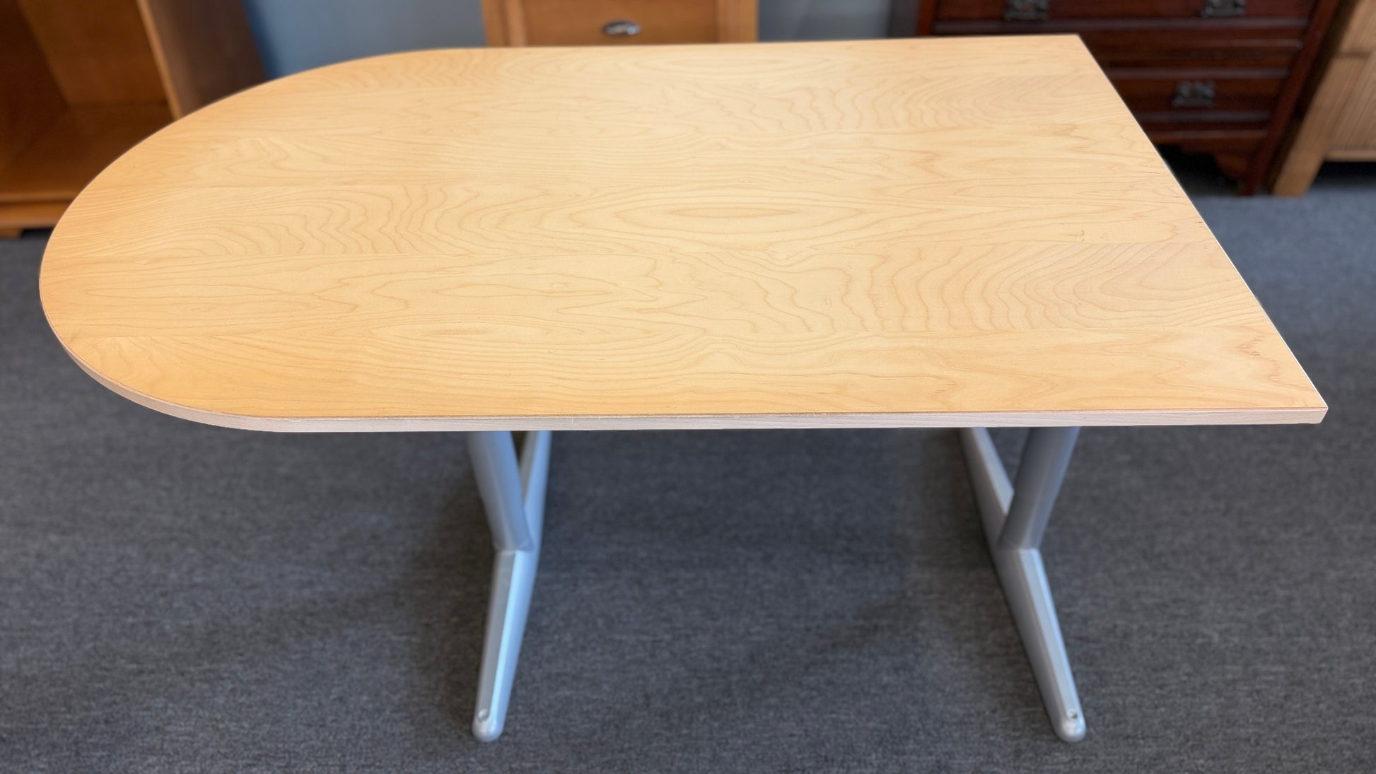 Modern office desk with a light wood D-shaped desktop, angled gray metal legs, and wide stabilizing feet.