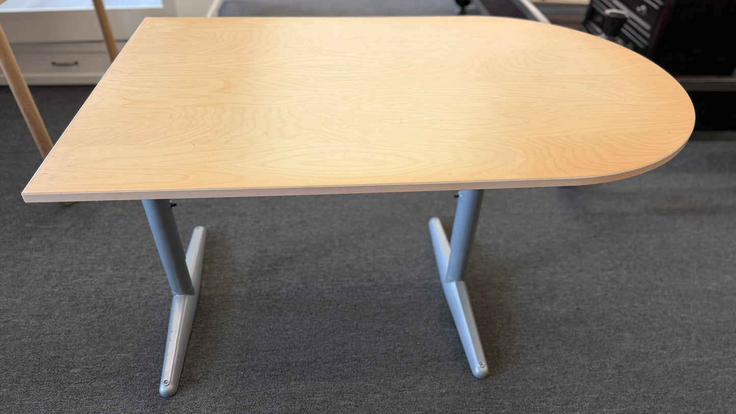 Modern office desk with a light wood D-shaped desktop, angled gray metal legs, and wide stabilizing feet.