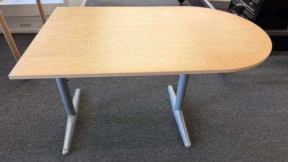 Modern office desk with a light wood D-shaped desktop, angled gray metal legs, and wide stabilizing feet.