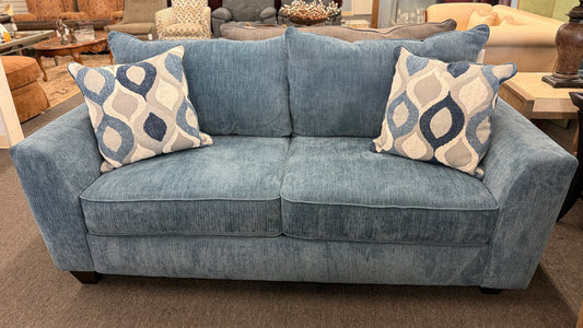 A plush two-seater sleeper loveseat upholstered in muted blue textured fabric with track arms, loose back cushions, and two geometric throw pillows.