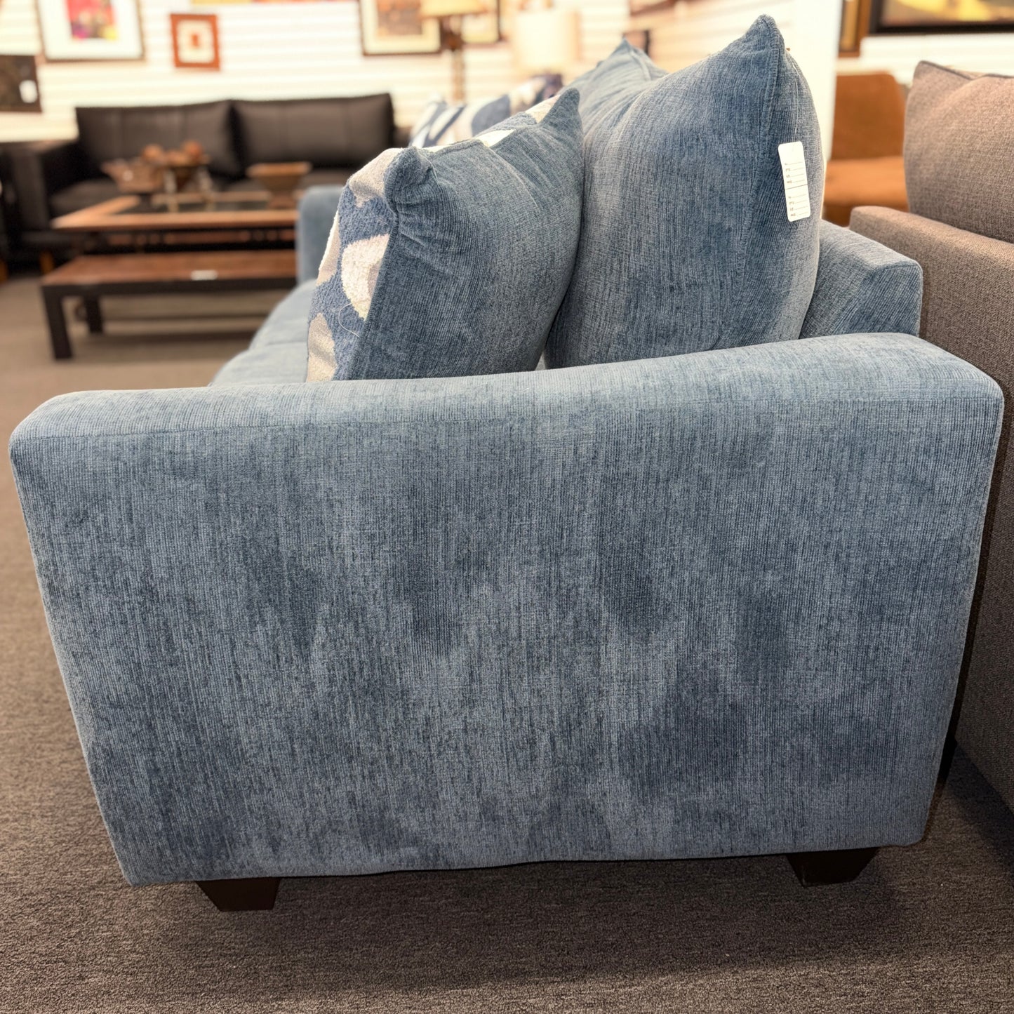 A plush two-seater sleeper loveseat upholstered in muted blue textured fabric with track arms, loose back cushions, and two geometric throw pillows.
