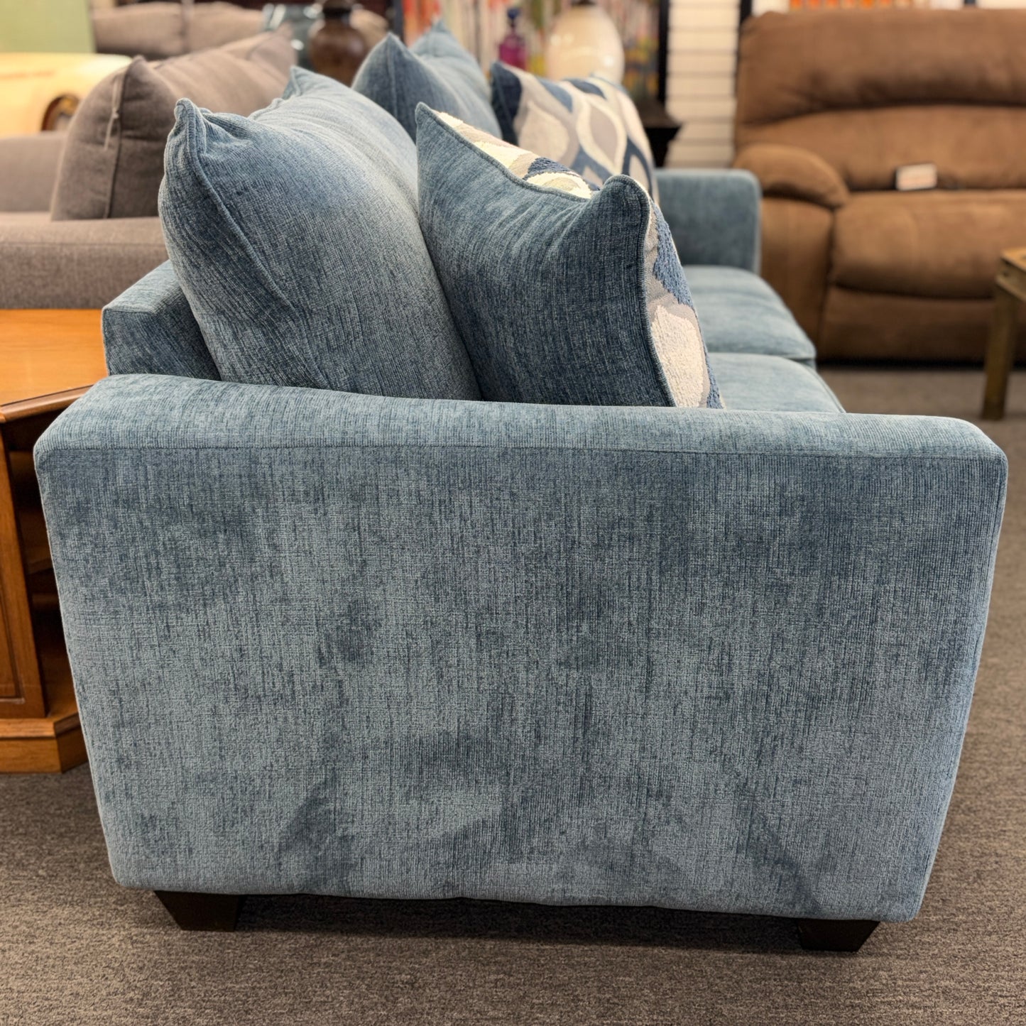 A plush two-seater sleeper loveseat upholstered in muted blue textured fabric with track arms, loose back cushions, and two geometric throw pillows.