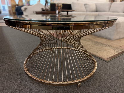 Modern round coffee table featuring a clear glass top and a sculptural flared wire-spoke metal base with a light, airy design.