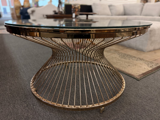 Modern round coffee table featuring a clear glass top and a sculptural flared wire-spoke metal base with a light, airy design.