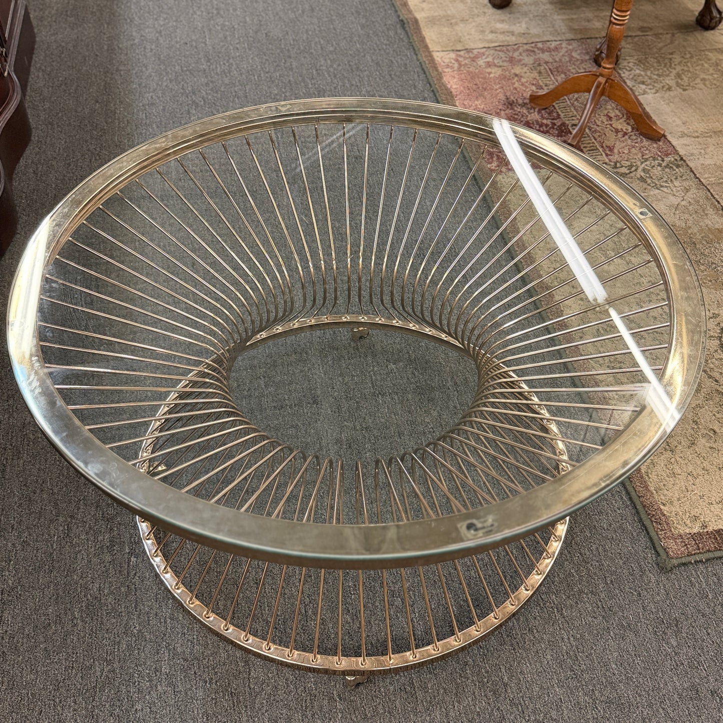 Modern round coffee table featuring a clear glass top and a sculptural flared wire-spoke metal base with a light, airy design.