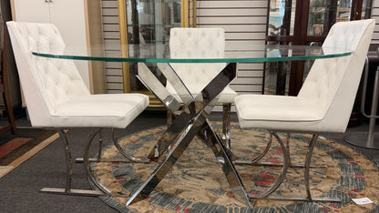 A modern dining set featuring a round glass-top table on an angled iron base with four white high-back tufted chairs.