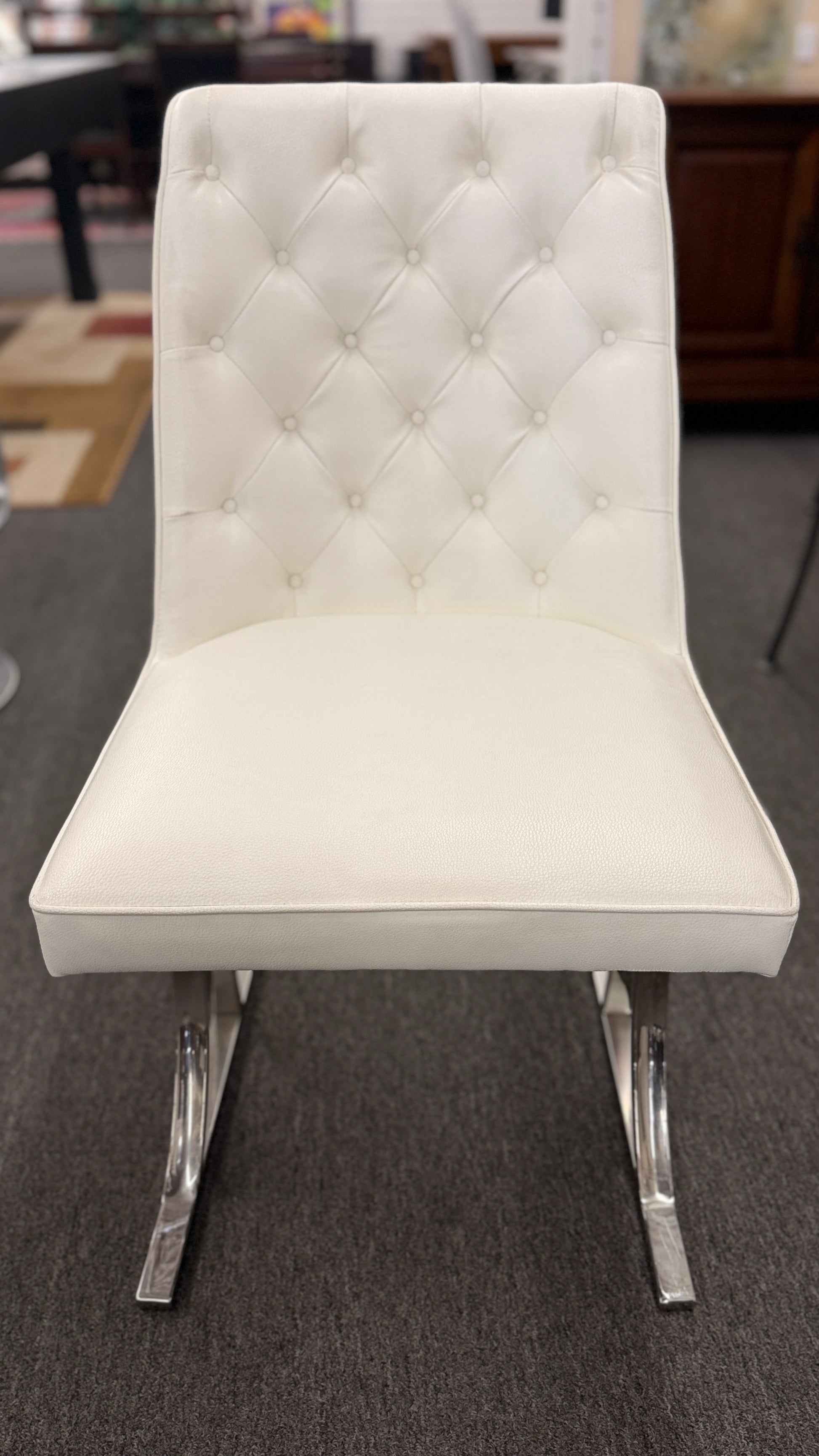 A modern dining set featuring a round glass-top table on an angled iron base with four white high-back tufted chairs.