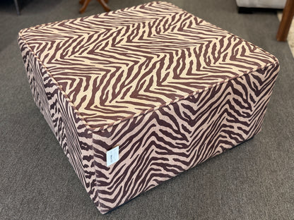 A modern square cube ottoman upholstered in a textured brown and beige zebra-stripe woven fabric in good condition.
