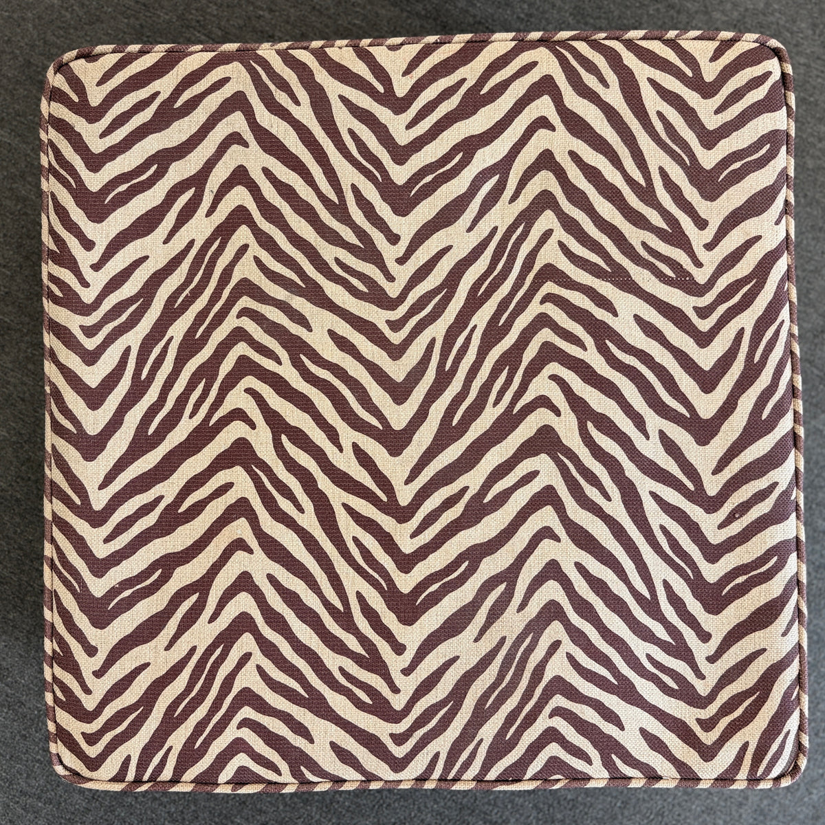 A modern square cube ottoman upholstered in a textured brown and beige zebra-stripe woven fabric in good condition.