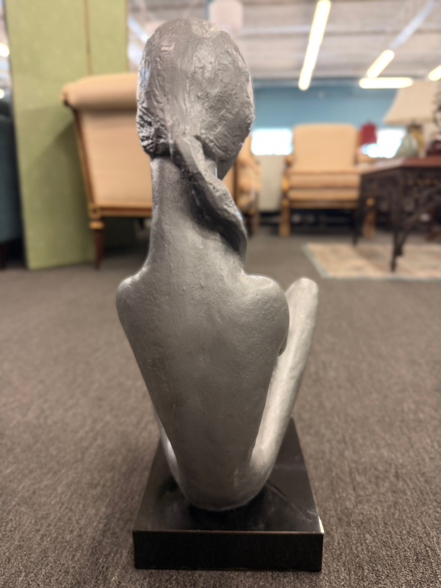 A stylized modern sculpture of a seated mother holding a young child with smooth elongated lines and a textured metallic finish mounted on a solid block base.