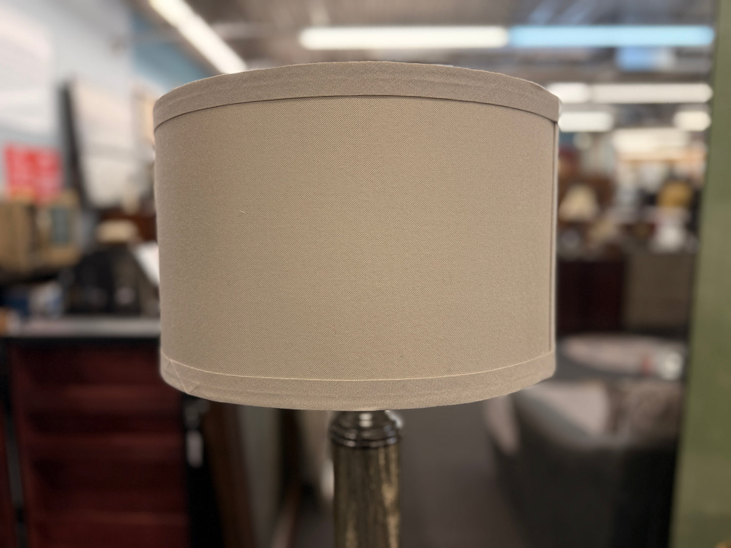 A tall floor lamp featuring a slender textured metallic column base and a neutral drum shade in excellent condition.