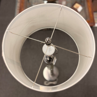 A tall floor lamp featuring a slender textured metallic column base and a neutral drum shade in excellent condition.