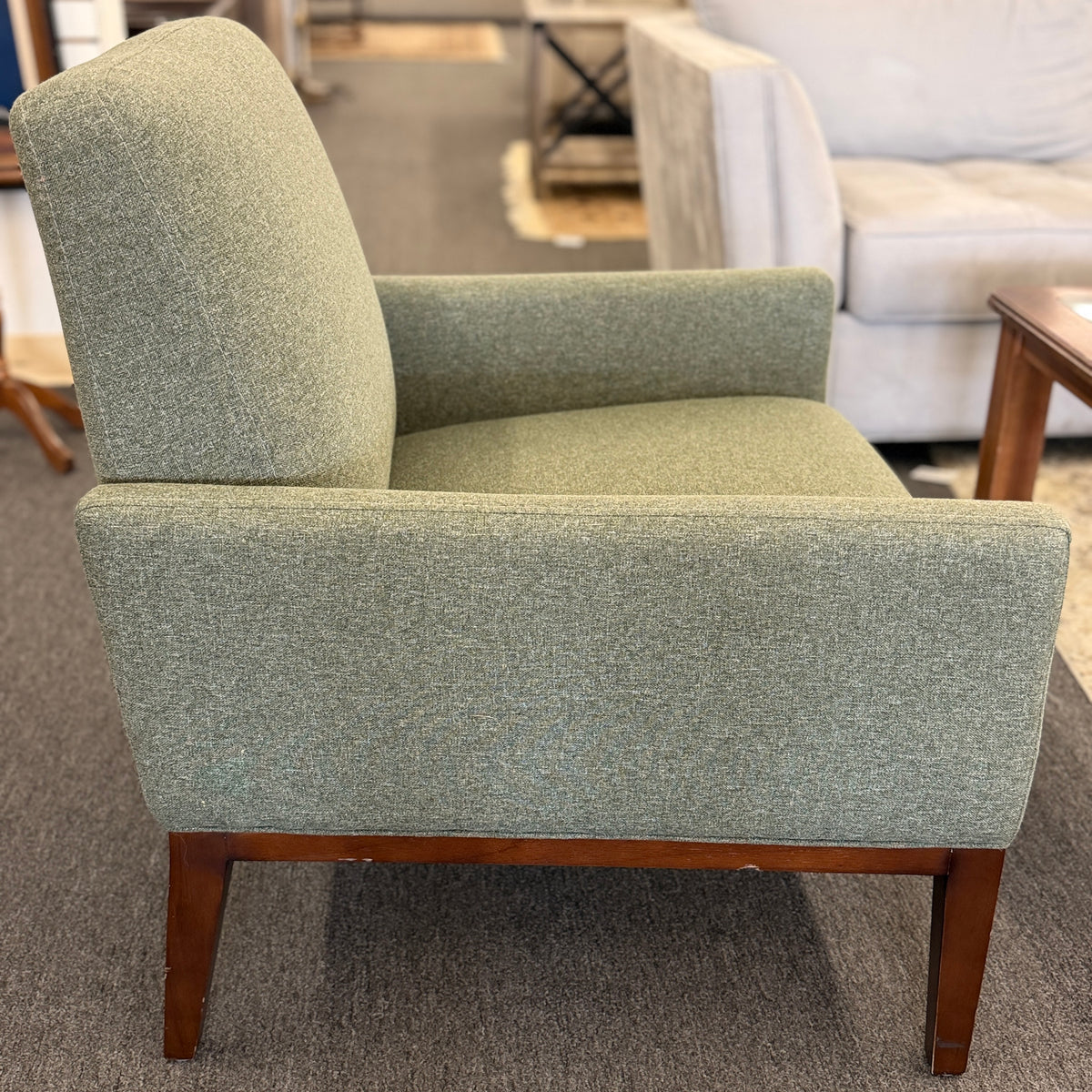 A modern transitional accent armchair upholstered in textured sage green woven fabric with track arms and tapered dark wood legs in good condition.