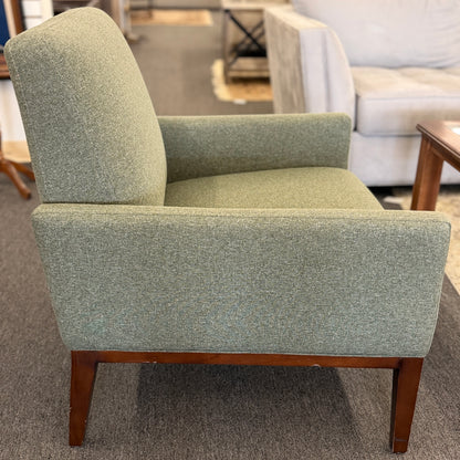 A modern transitional accent armchair upholstered in textured sage green woven fabric with track arms and tapered dark wood legs in good condition.