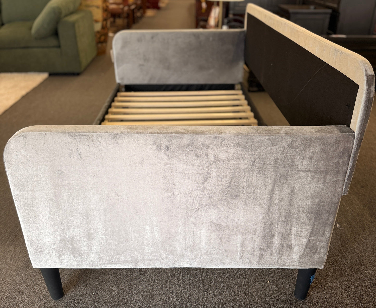 A modern daybed frame upholstered in a gray textured fabric, featuring a mid-height backrest, enclosed side panels, and a wooden slatted mattress support base.
