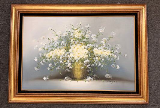 A traditional still-life canvas painting by Nancy Lee showing a dense bouquet of white daisies in a wicker basket, set in a dark velvet liner and an ornate gilded gold frame.
