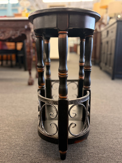 A narrow wooden accent table and magazine rack in a distressed black finish featuring turned spindle legs and scrolled metal side rails in good condition.