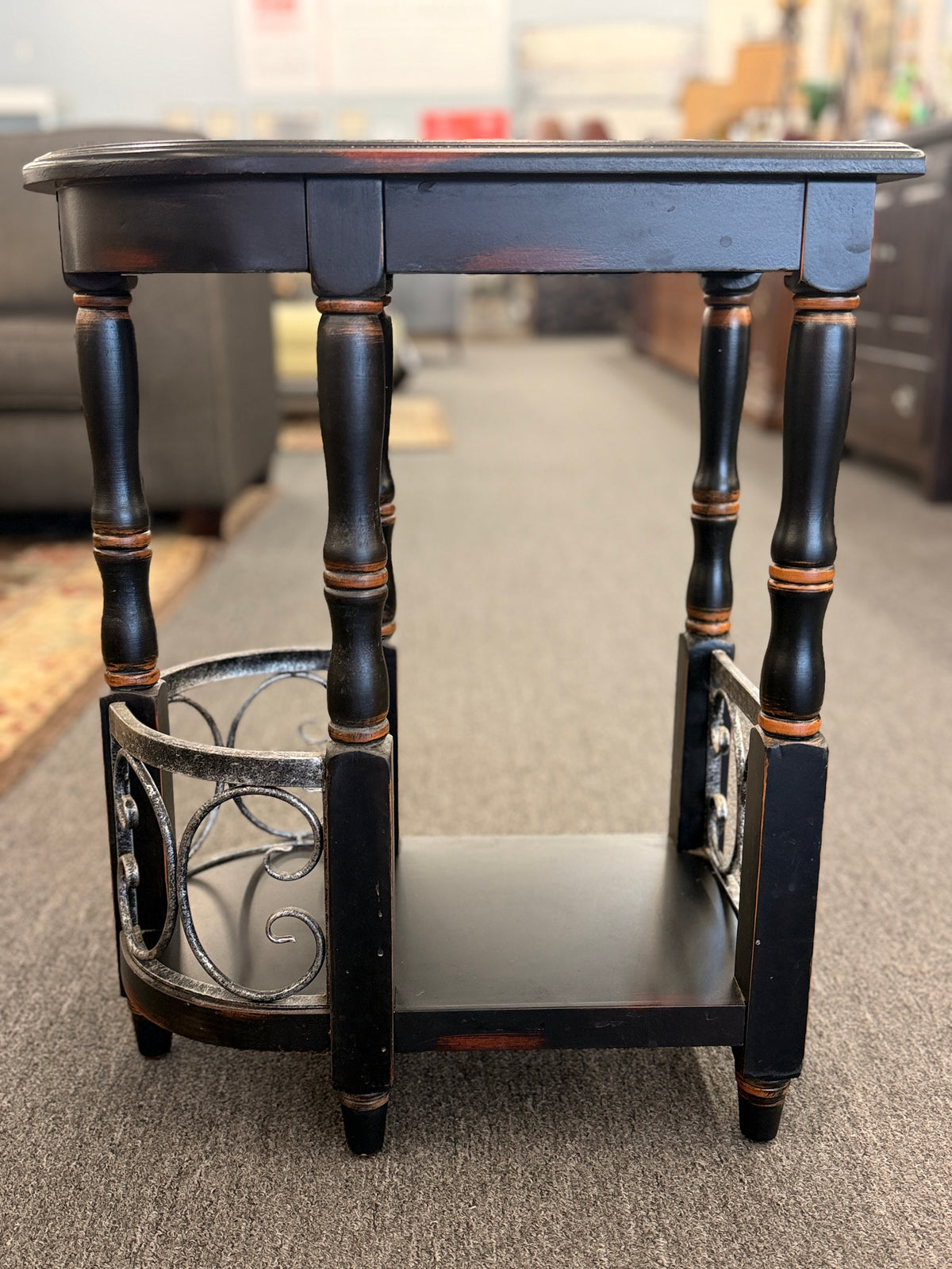 A narrow wooden accent table and magazine rack in a distressed black finish featuring turned spindle legs and scrolled metal side rails in good condition.