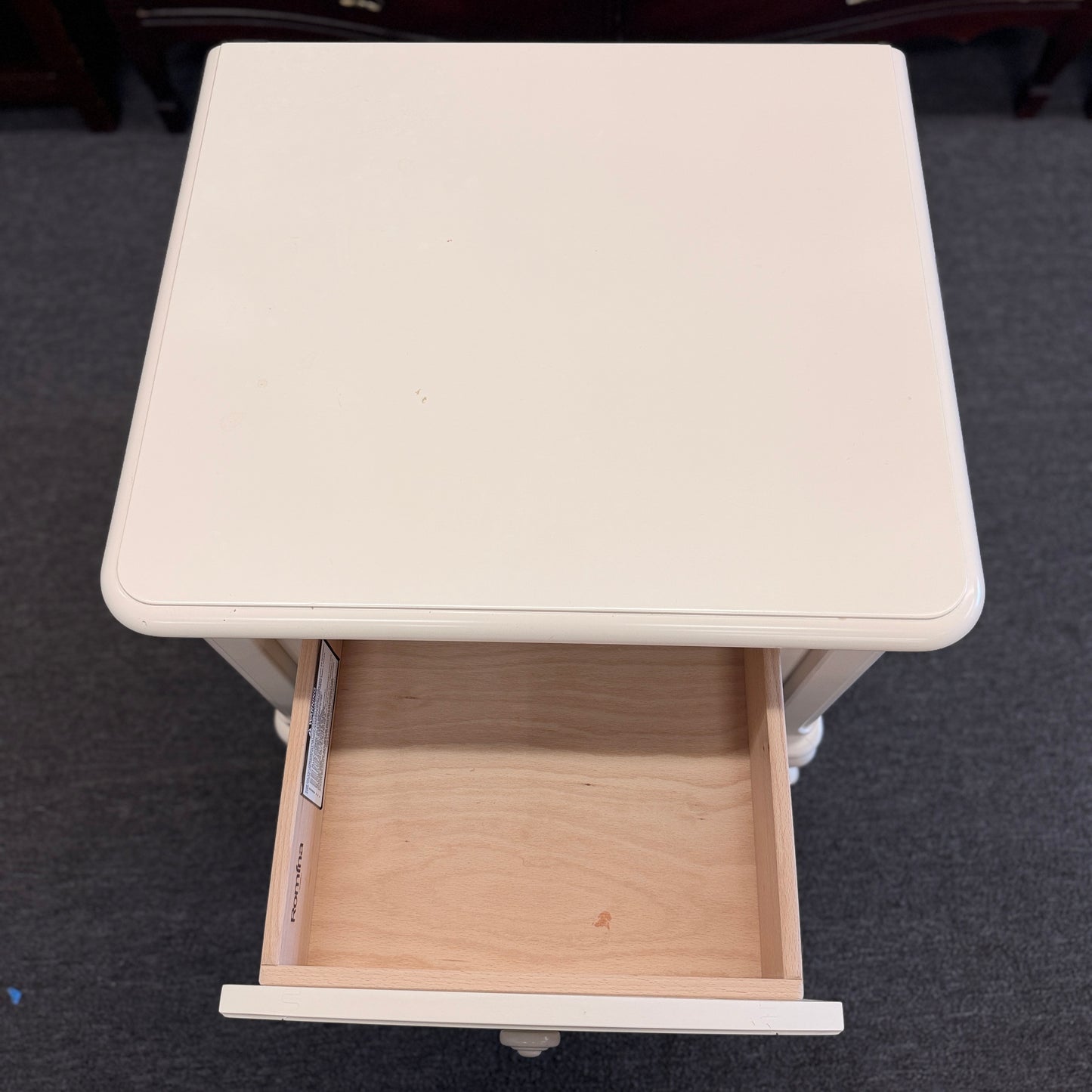 An off-white wooden nightstand featuring a single drawer with a turned knob, an open lower cubby, and curved cabriole legs.