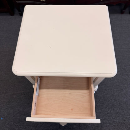 An off-white wooden nightstand featuring a single drawer with a turned knob, an open lower cubby, and curved cabriole legs.