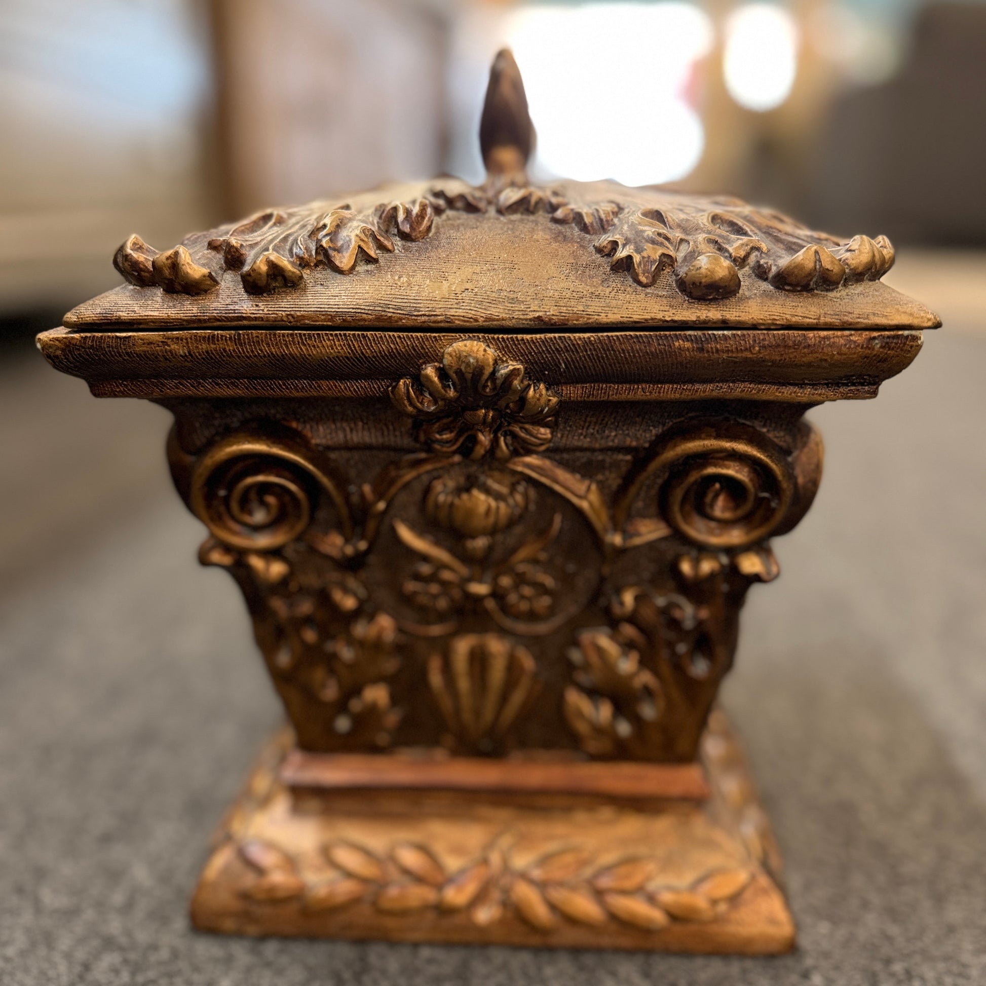 An ornate antique-style ceramic decorative box with a lid, featuring classical floral relief motifs and a distressed gold finish.