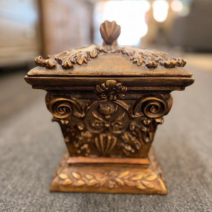 An ornate antique-style ceramic decorative box with a lid, featuring classical floral relief motifs and a distressed gold finish.