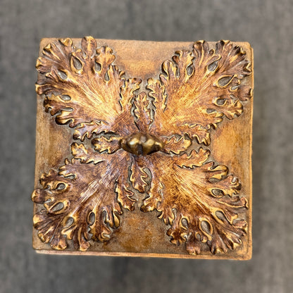 An ornate antique-style ceramic decorative box with a lid, featuring classical floral relief motifs and a distressed gold finish.
