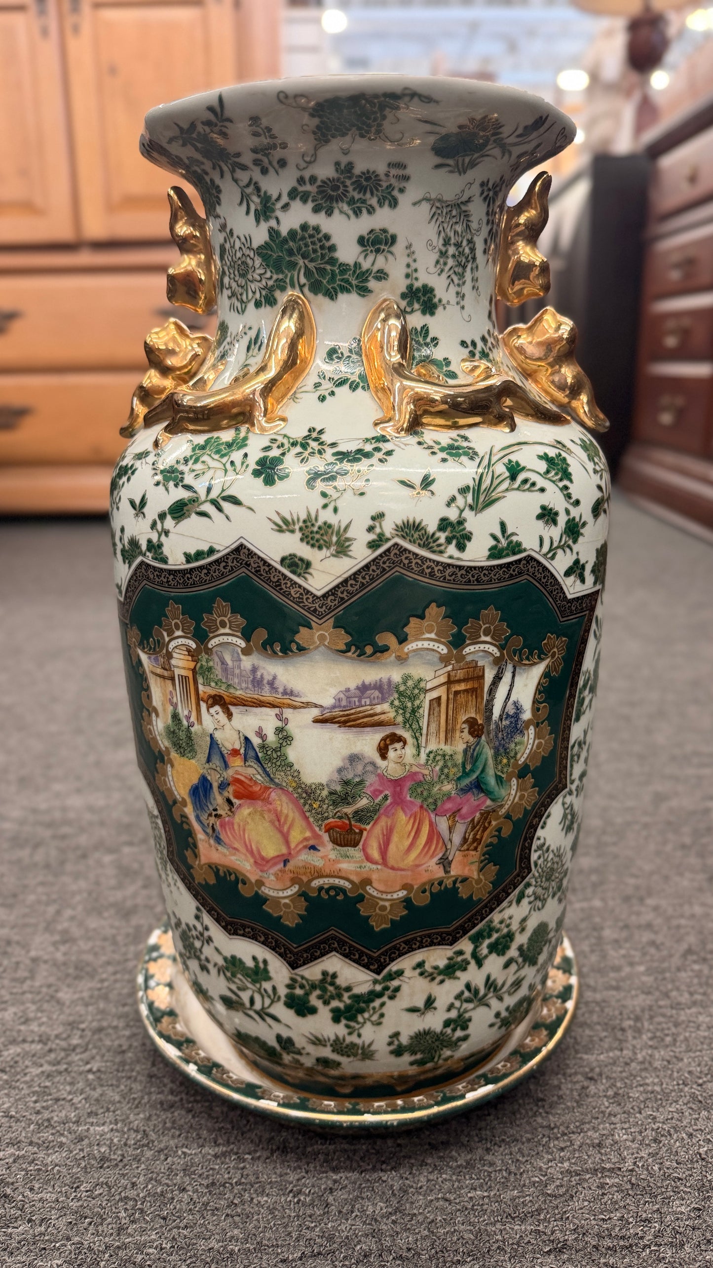 Tall ceramic vase with green and white floral patterns, sculpted gold-tone handles, a classical portrait medallion, and a matching pedestal saucer.