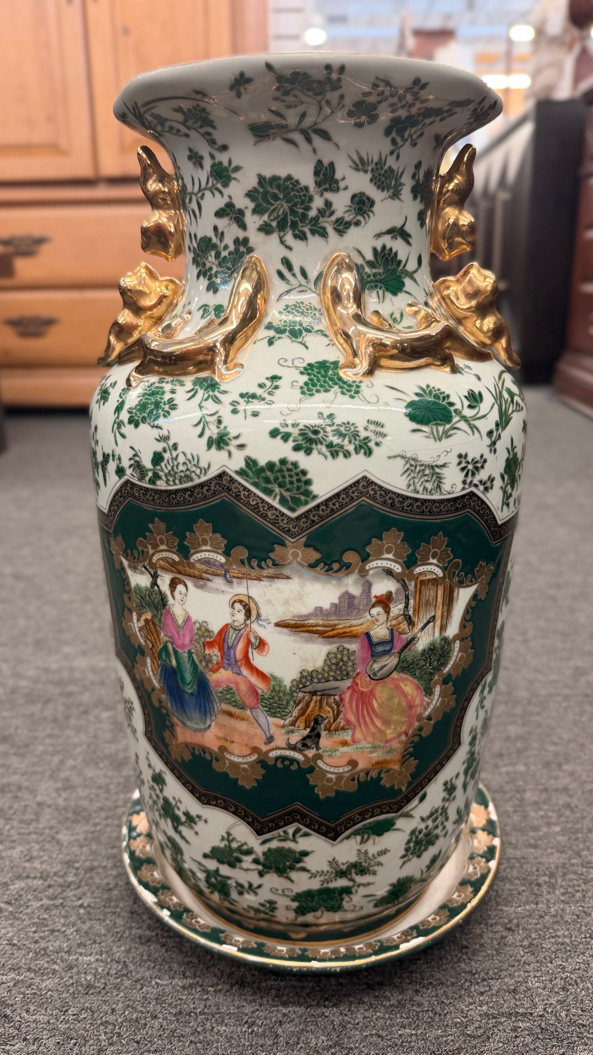 Tall ceramic vase with green and white floral patterns, sculpted gold-tone handles, a classical portrait medallion, and a matching pedestal saucer.