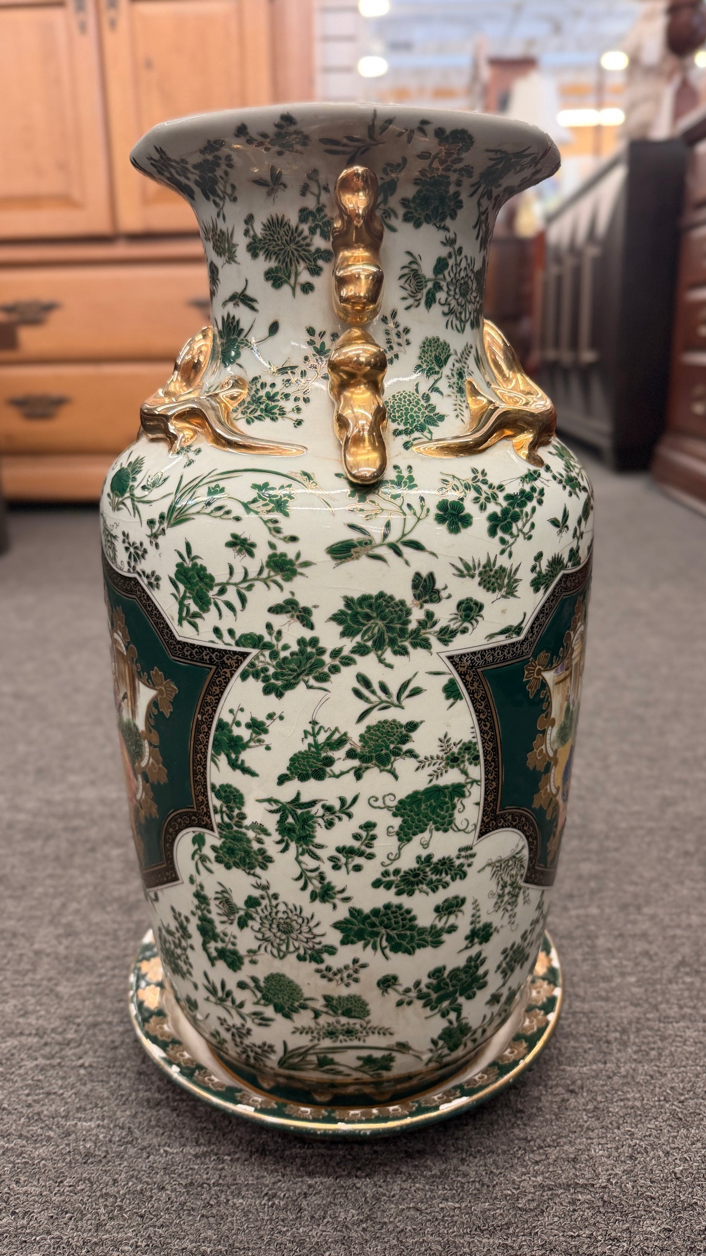 Tall ceramic vase with green and white floral patterns, sculpted gold-tone handles, a classical portrait medallion, and a matching pedestal saucer.