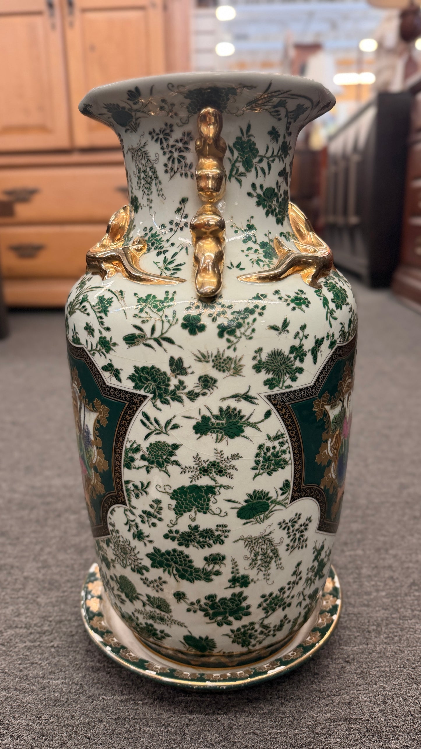 Tall ceramic vase with green and white floral patterns, sculpted gold-tone handles, a classical portrait medallion, and a matching pedestal saucer.