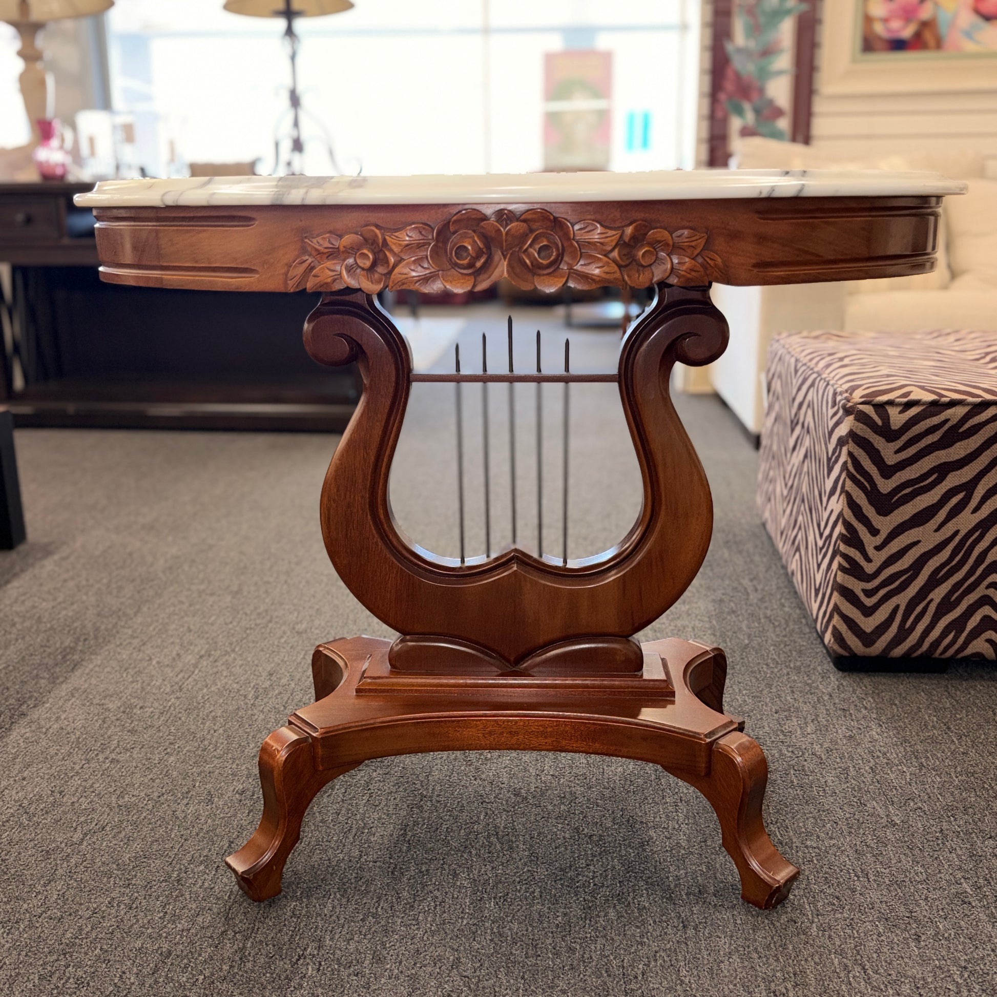 An ornate accent table featuring a white marble top, carved floral apron details, and a traditional lyre-shaped wooden base in excellent condition.
