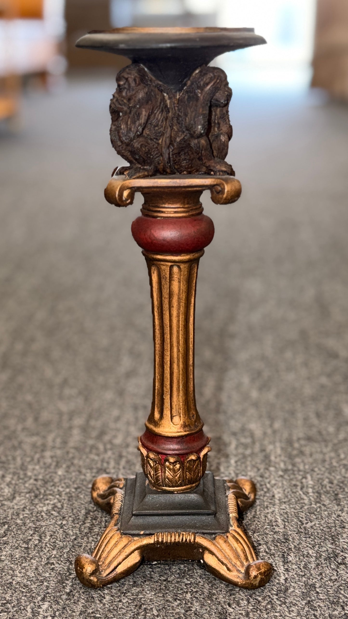 An ornate decorative ceramic candle holder with a fluted column base painted in antiqued gold and red tones, featuring a sculpted Three Wise Monkeys motif beneath the top tray.