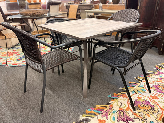 A 5-piece patio dining set featuring a square paneled top table with an umbrella hole and four dark woven resin wicker armchairs on iron frames.