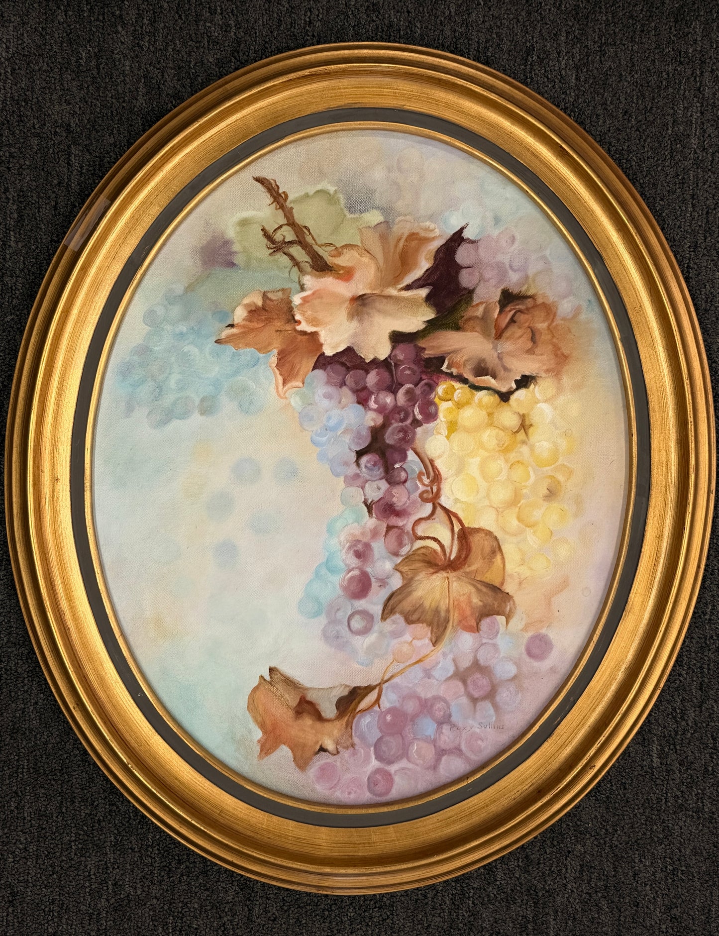 Oval framed still life artwork depicting a colorful cluster of grapes and leaves in soft pastel tones within a classic wooden frame.