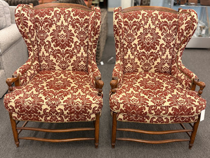 Pair of classic wingback armchairs upholstered in a bold burgundy and cream damask floral pattern detailed with nailhead trim and carved wooden legs in good condition.