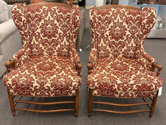 Pair of classic wingback armchairs upholstered in a bold burgundy and cream damask floral pattern detailed with nailhead trim and carved wooden legs in good condition.