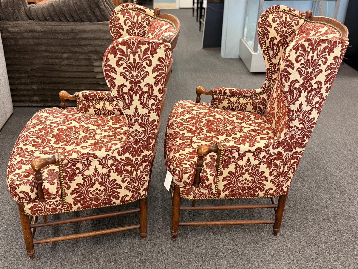 Pair of classic wingback armchairs upholstered in a bold burgundy and cream damask floral pattern detailed with nailhead trim and carved wooden legs in good condition.