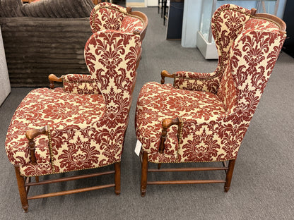 Pair of classic wingback armchairs upholstered in a bold burgundy and cream damask floral pattern detailed with nailhead trim and carved wooden legs in good condition.