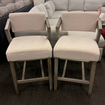 A pair of contemporary counter-height barstools featuring light oat upholstered seats and backs with angular weathered-wood frames in excellent condition.