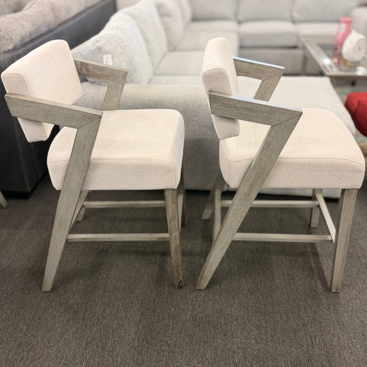 A pair of contemporary counter-height barstools featuring light oat upholstered seats and backs with angular weathered-wood frames in excellent condition.